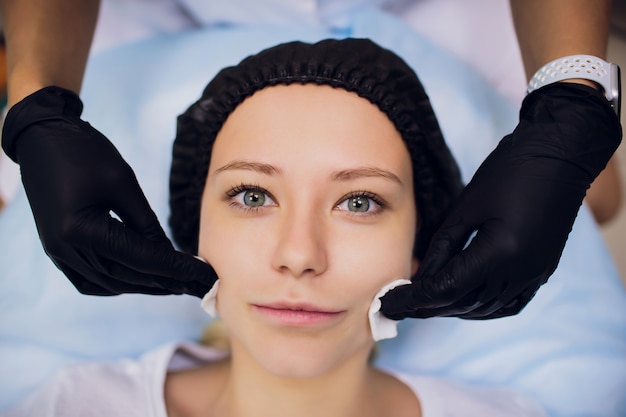 Pulire con la faccia di tovagliolo sterile. Giovane donna che riceve trattamenti nei saloni di bellezza.