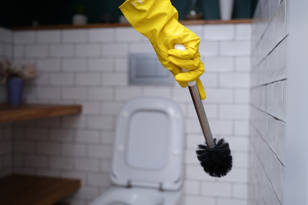 Pulitore in guanti di gomma gialli che tengono il primo piano dello scopino della toilette