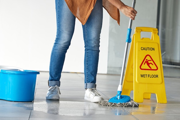 Pulizia del pavimento bagnato cautela e donna che pulisce nell'edificio per la salute o l'igiene della manutenzione Mop bidello servizio e pulitore con segnale di avvertimento o informazioni sulla sicurezza su piastrelle scivolose