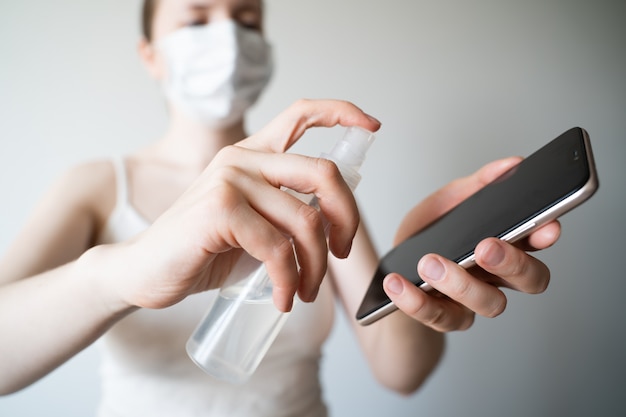 Pulizia del telefono cellulare per eliminare i germi, coronavirus Covid-19. La donna passa la pulizia dello smartphone dal disinfettante per le mani dell'alcool e pulisce con il panno