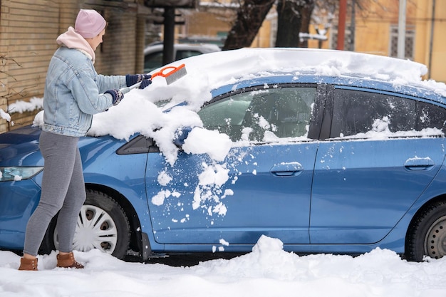 Pulizia della neve dal parabrezza, Raschiatura del ghiaccio, Pulizia invernale dei finestrini dell'auto. Donna che rimuove la neve dall'auto.