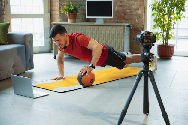 Pull up. Giovane uomo caucasico che si allena a casa durante la quarantena dell'epidemia di coronavirus, facendo esercizi di fitness, aerobico. Registrazione di video o streaming online. Benessere, sport, concetto di movimento.