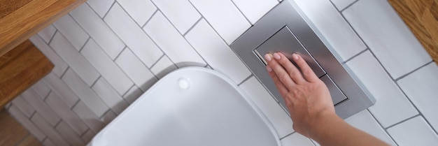 Pulsante di stampaggio a mano femminile per lo sciacquone della toilette in primo piano del bagno