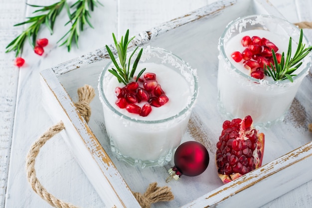 Punch al cocco di Natale con semi di melograno e rametti di rosmarino su superficie chiara