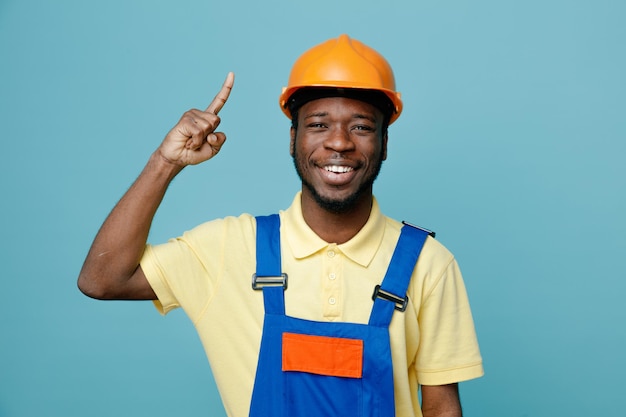 Punti impressionati su un giovane costruttore afroamericano in uniforme isolato su sfondo blu