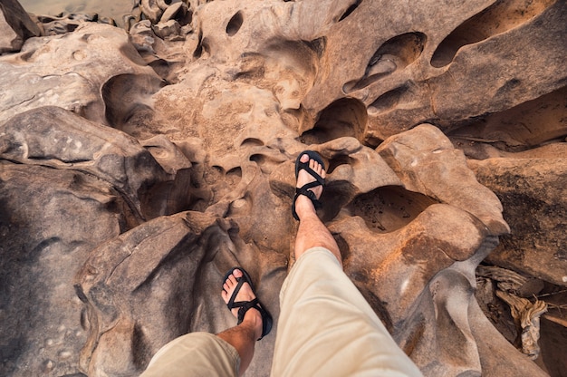 Punto di vista delle gambe dell'uomo con scarpe da trekking in piedi sulla robusta roccia del grand canyon in Thailandia