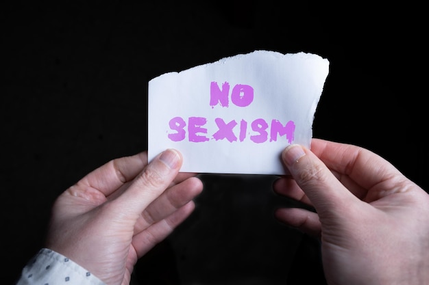 Punto di vista delle mani di una donna che tengono un foglio con la parola NO SEXISM scritta sopra