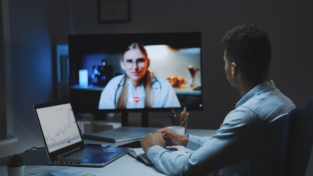 Punto di vista posteriore del giovane che fa videochiamata con il dottore capo sulla tua salute