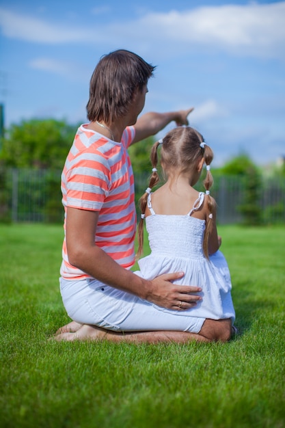 Punto di vista posteriore del padre con sua figlia che si siede nell'iarda all'aperto