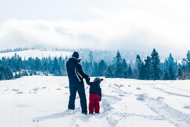 Punto di vista posteriore del ragazzino con il padre durante la vacanza sugli sci in montagna