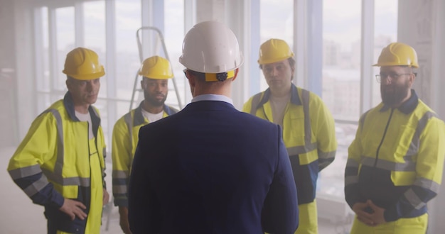 Punto di vista posteriore dell'uomo d'affari in vestito che parla alla squadra dei lavoratori edili