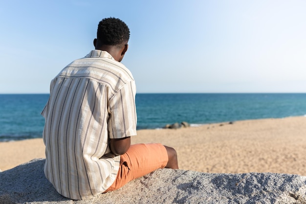 Punto di vista posteriore dell'uomo nero che si rilassa guardando l'oceano Spazio di copia