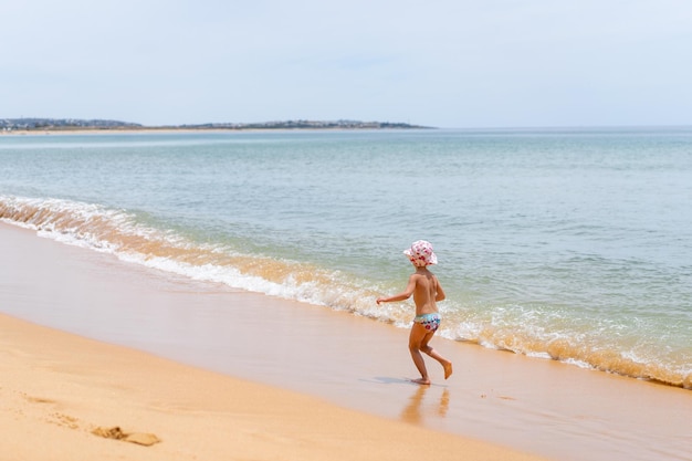 Punto di vista posteriore della bambina adorabile alla spiaggia sabbiosa dell'Oceano Atlantico durante l'estate
