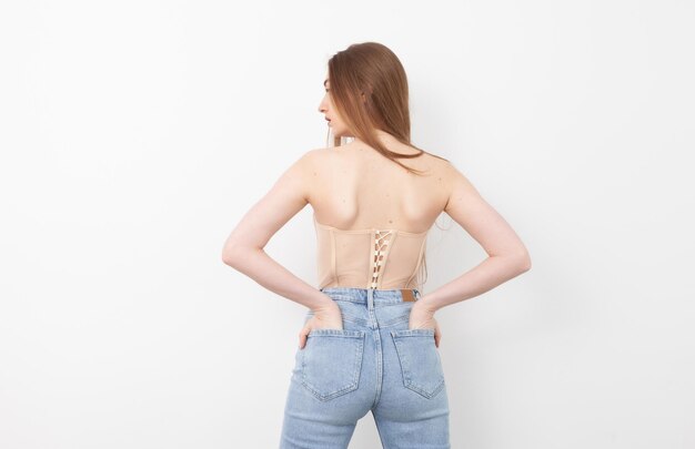 Punto di vista posteriore della donna alla moda sexy in jeans e corsetto su priorità bassa bianca