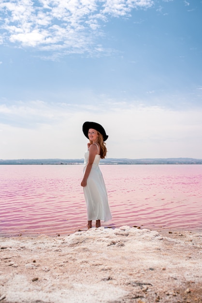 Punto di vista posteriore della donna sveglia dell'adolescente che porta vestito bianco che cammina su un lago rosa stupefacente