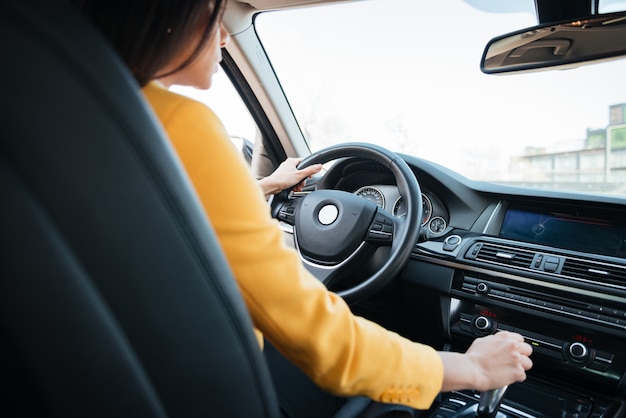 Punto di vista posteriore della giovane donna attraente che osserva sulla strada mentre guidando un'automobile