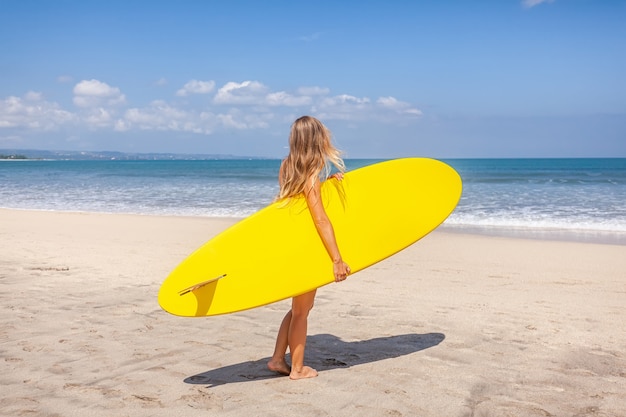 Punto di vista posteriore della giovane donna con capelli lunghi che tengono la tavola da surf che prepara navigare