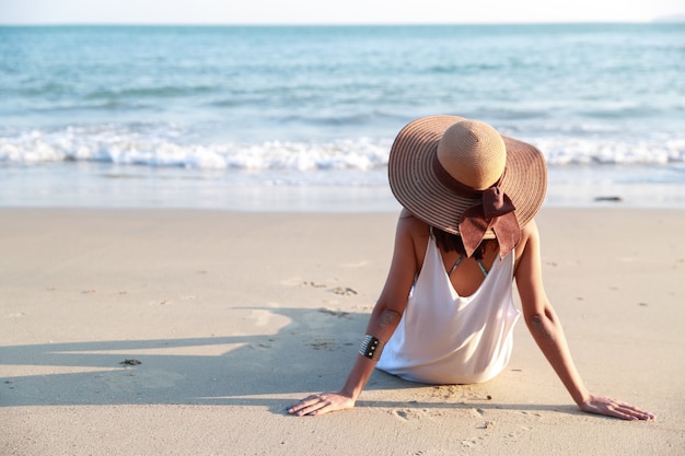 Punto di vista posteriore di bella ragazza asiatica con il cappello sulla spiaggia