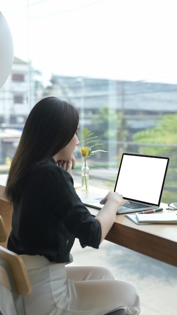 Punto di vista posteriore di giovane libero professionista femminile che lavora online con il computer portatile