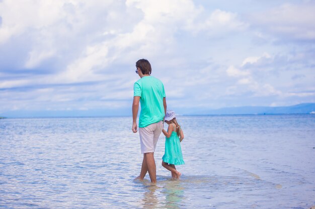 Punto di vista posteriore di giovane padre e della sua bambina che camminano vicino al mare