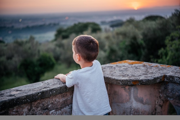 Punto di vista posteriore di un ragazzino che guarda il bel tramonto sull'oliveto nel paesaggio collinare dell'italia