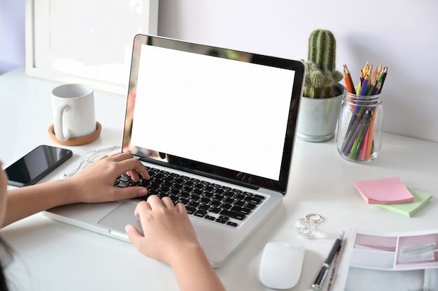 Punto di vista superiore del primo piano della femmina che lavora al computer portatile mentre sedendosi allo scrittorio bianco dell'area di lavoro