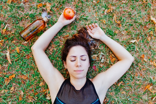 Punto di vista superiore della donna in buona salute che si trova sul sonno dell'erba. Giovane donna che tiene una mela prendersi cura della sua salute. Stile di vita sano per le persone in estate. Mangia una mela ogni giorno per una dieta equilibrata.