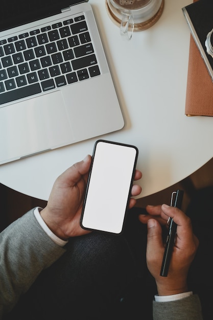 Punto di vista superiore di giovane uomo d'affari che tiene lo smartphone dello schermo in bianco mentre lavorando al suo progetto