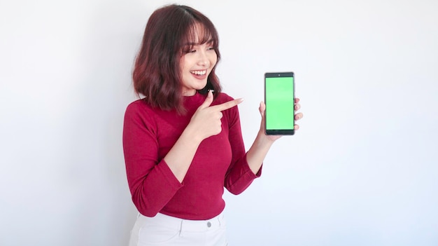 Punto felice della bella ragazza asiatica sul telefono dello schermo verde nella priorità bassa bianca