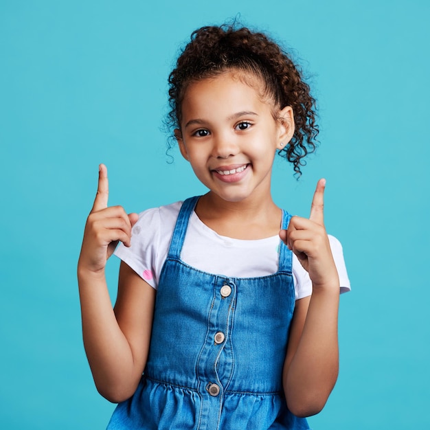 Punto ritratto e mockup con una ragazza su sfondo blu in studio che mostra lo spazio di posizionamento del prodotto Marketing e pubblicità per bambini con un'adorabile bambina che punta al marchio indoor