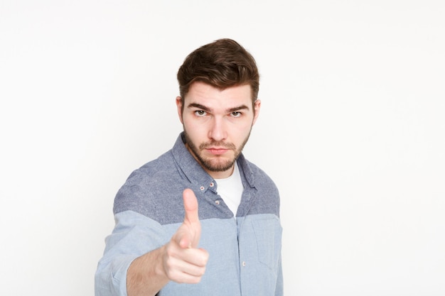 Punto serio rigoroso del giovane con il dito indice sulla macchina fotografica, fondo isolato bianco dello studio. Poster di motivazione