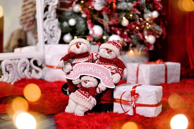 Pupazzo di neve con regali di Natale e albero di Capodanno e bokeh leggero sullo sfondo. Traduzione: "Felice anno nuovo!"