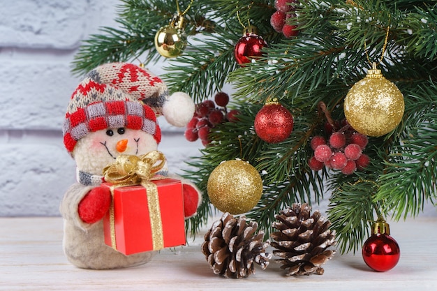 Pupazzo di neve di Capodanno con regalo sullo sfondo dell'albero di Natale