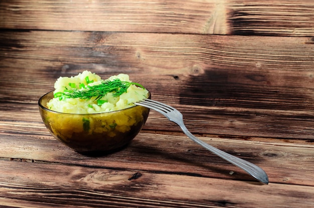 Purè di patate con aneto verde in ciotola di vetro su tavola di legno