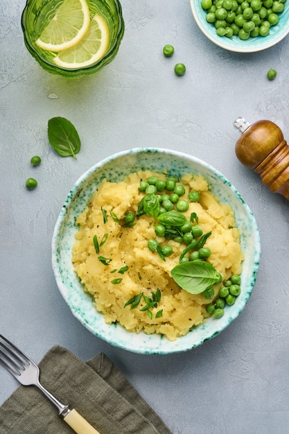 Purè di patate con burro, piselli, cipolle, basilico in una ciotola bianca su sfondo chiaro di ardesia, pietra o cemento