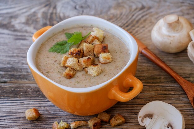 Purea di zuppa con funghi e crostini di pane in una ciotola arancione su un tavolo di legno