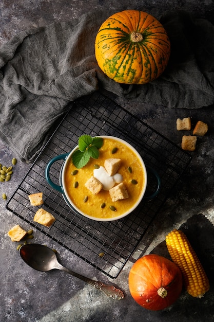 Purea di zuppa di zucca tradizionale con cracker, panna e semi in una ciotola, su uno sfondo scuro Copia spazio