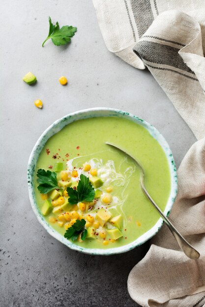 Purea di zuppa tenera fatta in casa da avocado e mais con crema in piatto di ceramica rustico sulla vecchia superficie di cemento grigio. Messa a fuoco selettiva. Vista dall'alto.