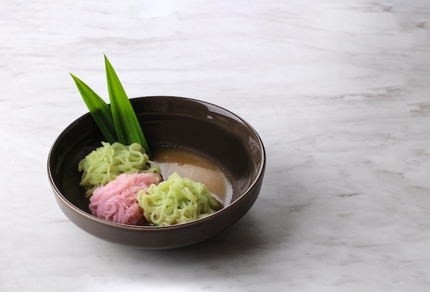 Putu Mayang o Petulo, spuntino tradizionale giavanese indonesiano fatto di fili di farina di riso arricciati in una palla con colorante alimentare, servito con latte di cocco e sciroppo di zucchero di palma. Sfondo bianco