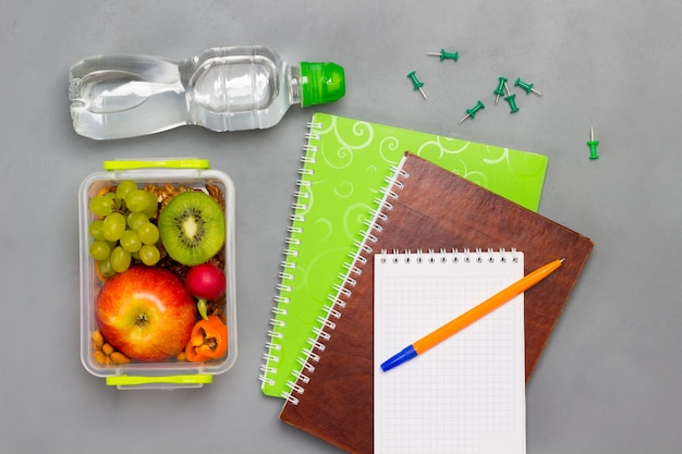 Quaderni e penna, lunch box con frutta e noci e bottiglia d'acqua