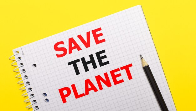 Quaderno bianco con scritta SAVE THE PLANET scritta a matita nera su sfondo giallo brillante.