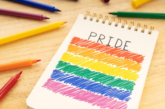 Quaderno con disegno della bandiera arcobaleno LGBT e penne di marcatura su un tavolo di legno