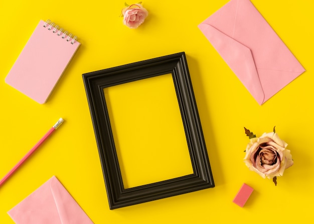 quaderno dello spazio pastello e cornice nera con fiore rosa e matita su sfondo giallo