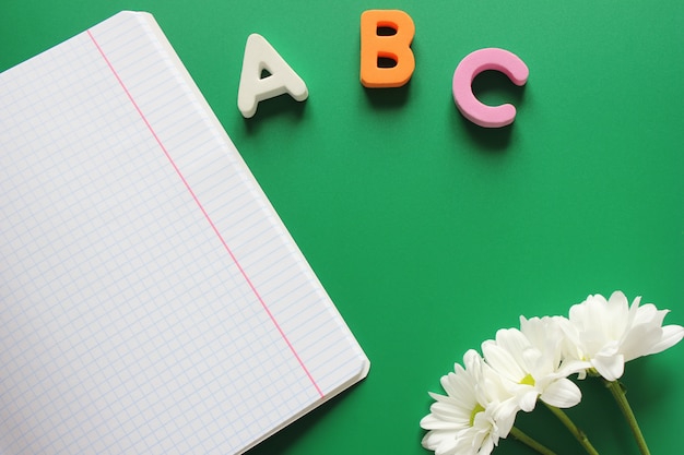 Quaderno di scuola accanto alle lettere ABC e crisantemi bianchi