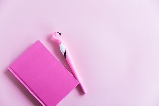 Quaderno rosa per appunti divertente penna fenicottero su sfondo rosa pastello Disposizione piatta Vista dall'alto Copia spazio