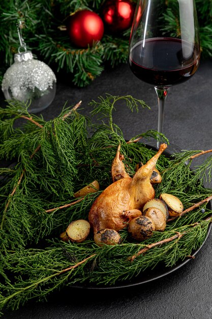 Quaglia fritta su un piatto decorato con rami verdi con un bicchiere di vino rosso su uno sfondo scuro di natale