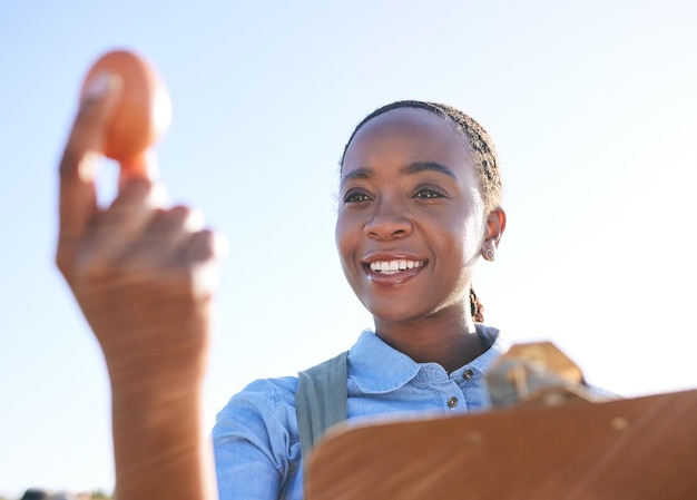 Qualità della donna e uova in mano in fattoria con appunti all'esterno per piccole imprese sostenibili in Africa Lista di controllo per l'ispezione dell'allevamento di pollame e felice agricoltore nero in campagna con cielo e sorriso