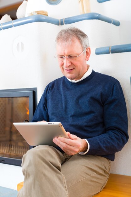 Qualità della vita - Uomo anziano o pensionato seduto a casa davanti alla fornace, scrivendo e-mail sul tablet o leggendo un e-book