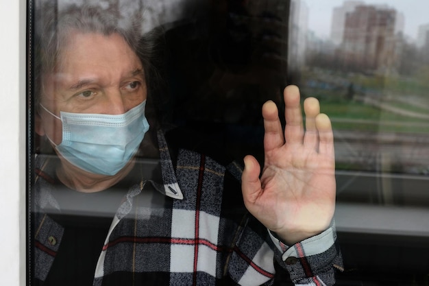 Quarantena di auto-isolamento uomo anziano solitario che indossa una maschera medica guarda attraverso la finestra a