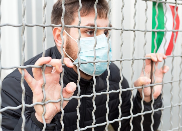 Quarantena italiana, stop coronavirus. Focolaio di diffusione di coronavirus in Italia. Covid-19 in Europa UE. Uomo in maschera protettiva medica con bandiera italiana in gabbia